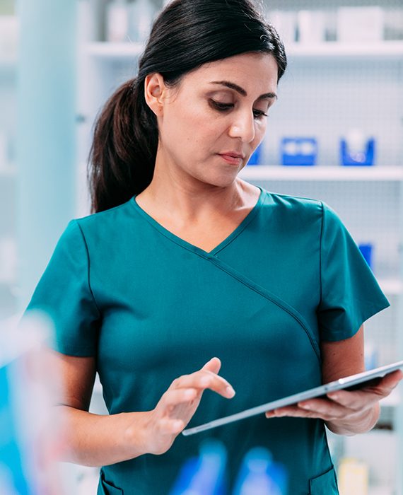 Female pharmacist consults tablet device in front of medication storage cabinet