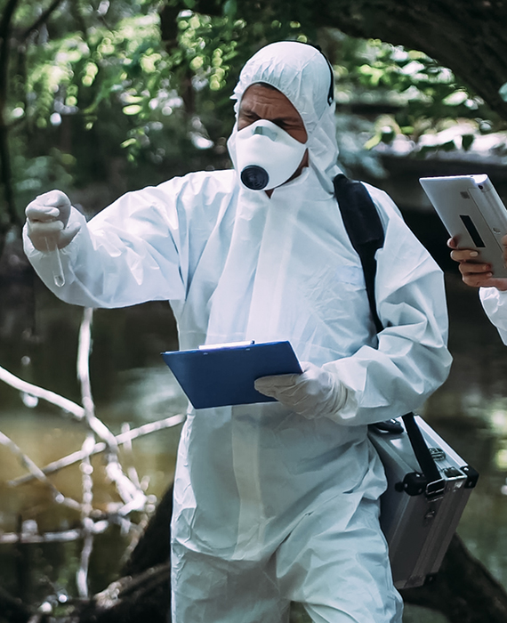 Researchers in protective suits take river water samples using test tubes and tablet devices
