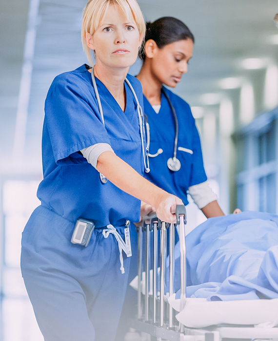 Two nurses wheel patient down hospital corridor on gurney