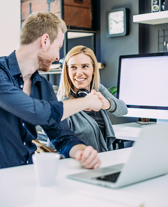 Two software developers performing fist bump in modern office setting