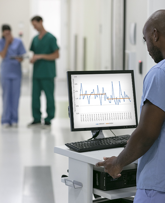 Male nurse using ICNET software at workstation in busy hospital corridor